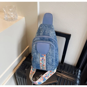 Detail of vintage denim crossbody bag with colorful floral embroidered strap on a suitcase