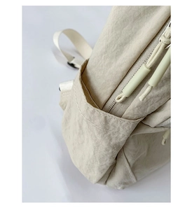Detail view of the crinkled nylon fabric and side pocket on the beige shoulder bag