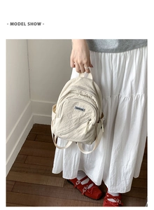 Detail shot of beige wrinkled canvas backpack showing adjustable straps and logo label