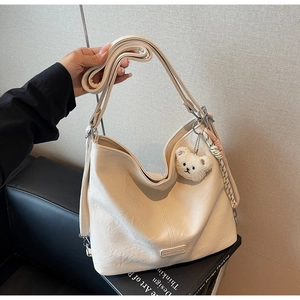 Detail of creamy white faux leather tote bag with plush bear charm and adjustable strap