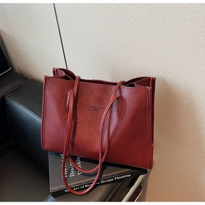 Detailed close-up of dark red leather tote bag showing embossed text and zipper closure