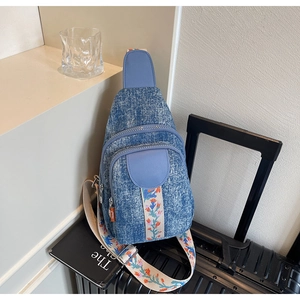 Detail of blue denim crossbody bag featuring an intricate floral embroidered wide strap