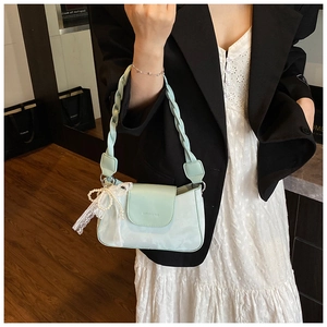 Detail of mint green shoulder bag featuring a woven strap and lace bow pearl charm