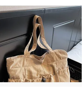 Detail of beige tote bag showing adjustable drawstring side pockets and wide strap