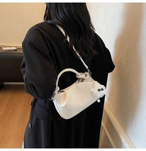 Creamy white pleated cloud bag with knotted handle and plush charm on female model