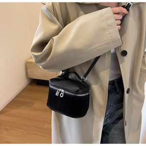 Detail of a black textured crossbody bag styled with a khaki coat and blue denim jeans