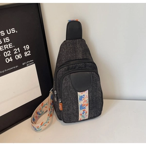 Detail view of dark grey denim chest bag with colorful ethnic style embroidered strap