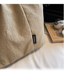 Close-up of beige tote bag featuring crinkled texture fabric and a woven SHUNUO side label