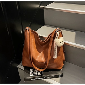 Close-up of caramel brown tote bag with pebble leather texture and plush bear pendant