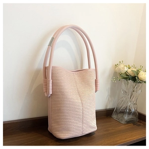 Close-up of pink woven bucket bag texture with leather handles on a wooden table