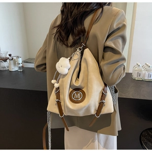Dettaglio della borsa tote scamosciata beige con logo M, cinturini in pelle e ciondolo