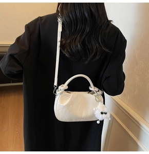 Rear view of a textured off-white cloud bag with a plush charm and adjustable strap