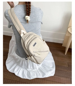 Close-up of off-white canvas chest bag with multiple zippers and brand label
