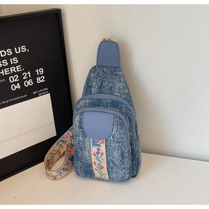 Detail of blue denim sling bag featuring floral embroidered wide strap and double zippers
