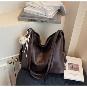 Close-up of vintage brown leather tote bag with logo detail and cute bear charm