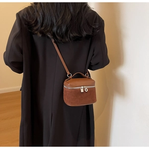 Detailed view of brown leather box-shaped crossbody bag worn by a model in a minimalist room