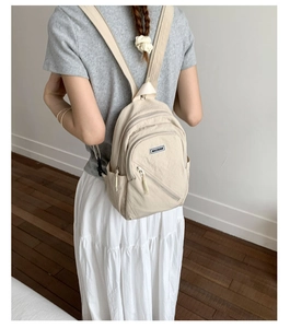 Detail view of cream-white mini backpack with multi-layer zippers and side water bottle pocket