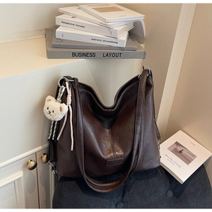 Detail of chocolate brown PU leather tote bag with plush bear charm and vintage books