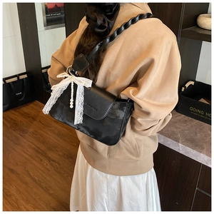 Detail of black crossbody bag with white lace bow, pearl charm, and woven rope strap
