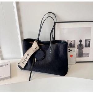Macro detail of black quilted faux suede tote bag with minimalist logo tag and coin purse