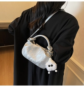 Silver metallic cloud bag with fluffy monster charm shown from a back view on a model