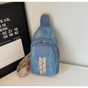 Detail of blue denim sling bag featuring retro floral embroidery on the strap and pocket