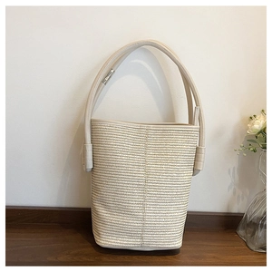 Detail view of woven straw bucket bag with cream leather handle on a wooden table