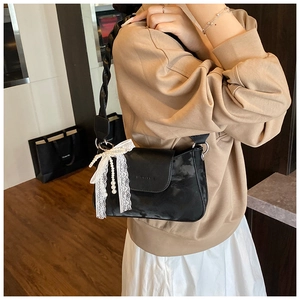 Detail view of black underarm bag featuring a white lace bow and elegant pearl charm