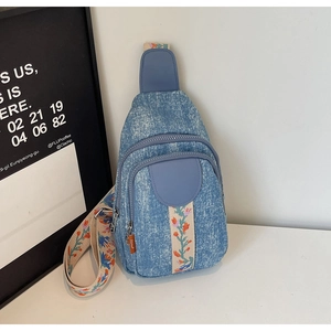 Detail of blue denim crossbody bag featuring floral embroidery strap and leather flap