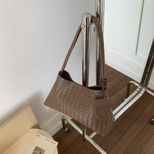 Dettaglio di una borsa a secchiello intrecciata marrone appesa a un gancio in metallo