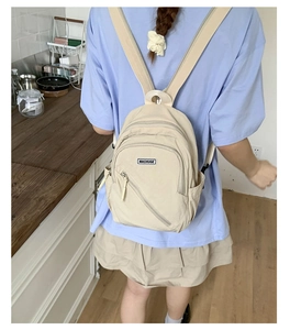 Close-up of beige fabric backpack with multi-layer zippers and woven MACHUGE label