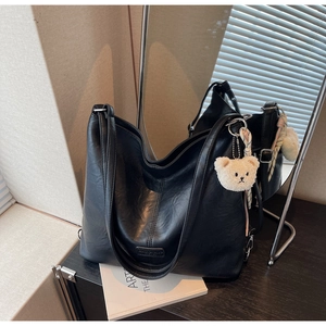 Detail of black faux leather tote bag with silver hardware and a beige plush bear charm