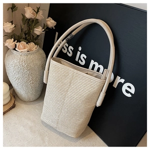 Detail of cream woven bucket bag with dual handles and fabric lining on a soft fabric base