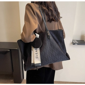 Detail of black quilted tote bag featuring a decorative ribbon and a small round pouch