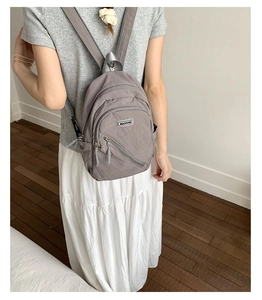 Detail of a gray mini nylon backpack showing multi-zipper pockets and fabric brand label