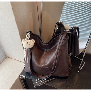 Detail of deep brown textured leather tote bag with a cute plush bear charm accessory
