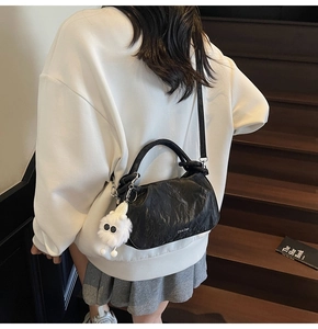Detail of black pleated crossbody bag with white plush monster charm on stairs