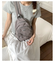 Close-up of gray nylon chest bag with multiple zippers and brand label worn by model