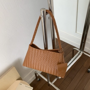 Dettaglio borsa a secchiello in pelle intrecciata color cuoio con ciondolo rotondo