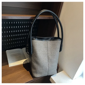 Detail of woven bucket bag with black leather handle on a wooden bookshelf background