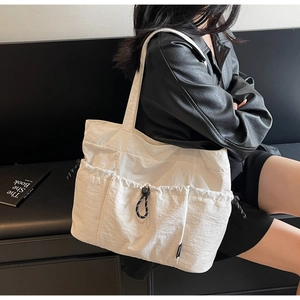 Detail of white nylon tote bag featuring multiple utility pockets with black drawstring cords