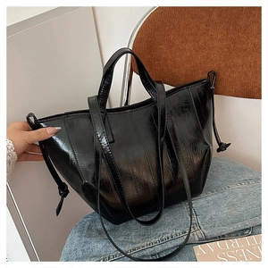 Detail of black glossy wrinkled tote bag with decorative side drawstrings on denim
