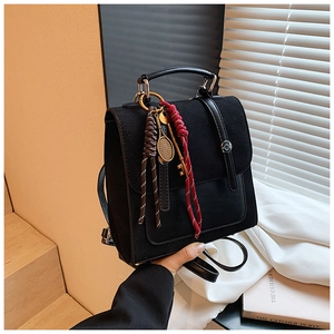 Detail of black faux leather backpack featuring tennis racket charm and woven pendant