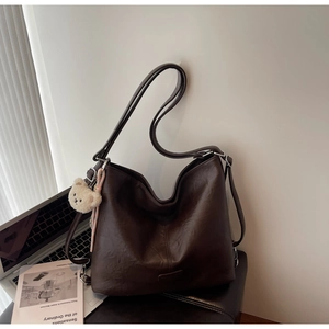 Detail of dark brown tote bag with high-quality leather texture and cute plush bear charm