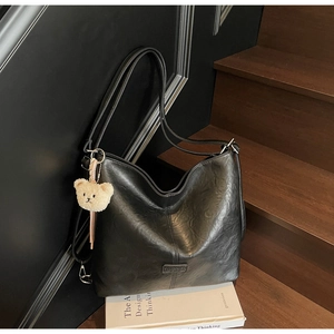 Detail of black leather tote bag with vertical stitching and cute plush bear charm