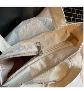 Detail view of a cream canvas tote bag showing smooth silver metal zipper closure and texture