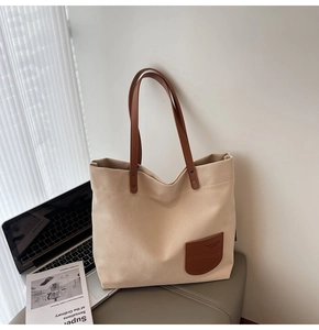 Dettaglio borsa tote in tela beige con tasca frontale in pelle marrone e manico