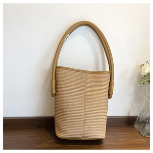Close-up of woven straw bucket bag featuring a premium brown leather handle on wood