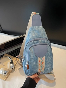 Light blue denim crossbody bag with floral embroidery on white tabletop setup