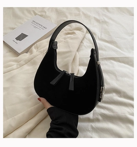 Detail of black suede hobo bag with dual zipper closure on a white fabric background
